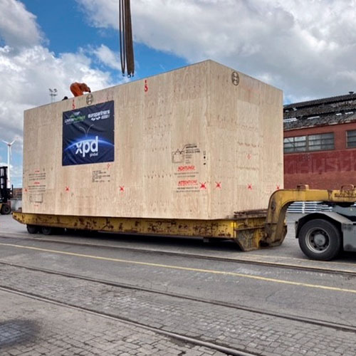 Our Project cargo wooden box branded with xpd global logo being moved inside the German port over a special platform. Nuestra carga sobredimensionada protegida por una caja de madera con el logo de xpd global siendo transportada adentro del puerto sobre una plataforma especial.